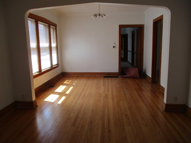 spare room featuring a notable chandelier, arched walkways, crown molding, and wood finished floors