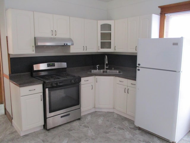 kitchen with a sink, stainless steel gas range, dark countertops, freestanding refrigerator, and under cabinet range hood