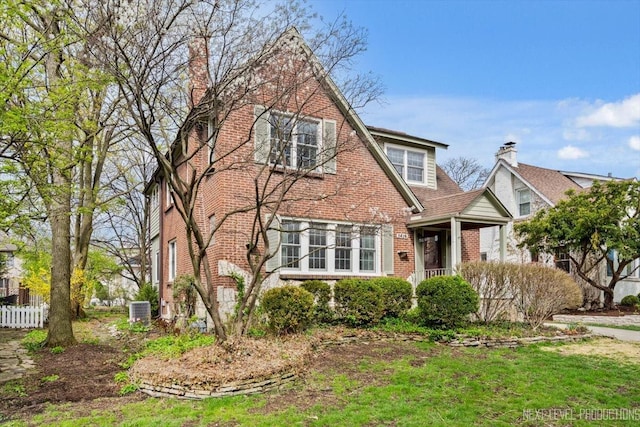 tudor-style house with brick siding, a chimney, central AC unit, and fence