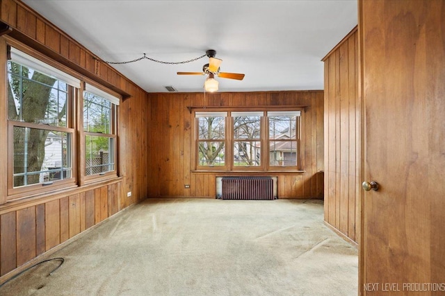 carpeted empty room featuring plenty of natural light, wood walls, and radiator