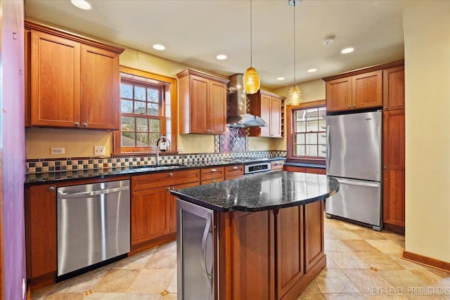kitchen with stainless steel appliances, a sink, recessed lighting, wall chimney range hood, and a kitchen island