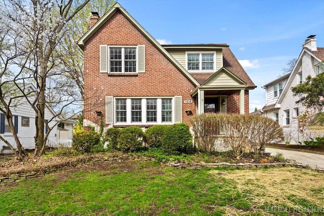 view of front of house featuring a chimney, a front lawn, and brick siding