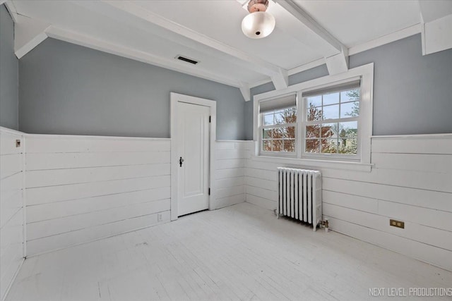 spare room with beamed ceiling, radiator heating unit, visible vents, and a wainscoted wall