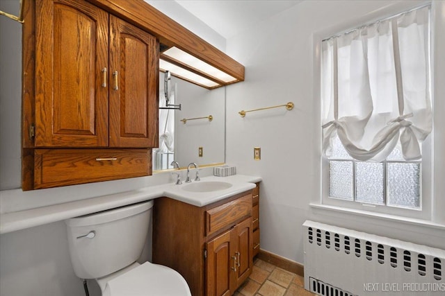 bathroom featuring toilet, stone tile floors, baseboards, radiator heating unit, and vanity