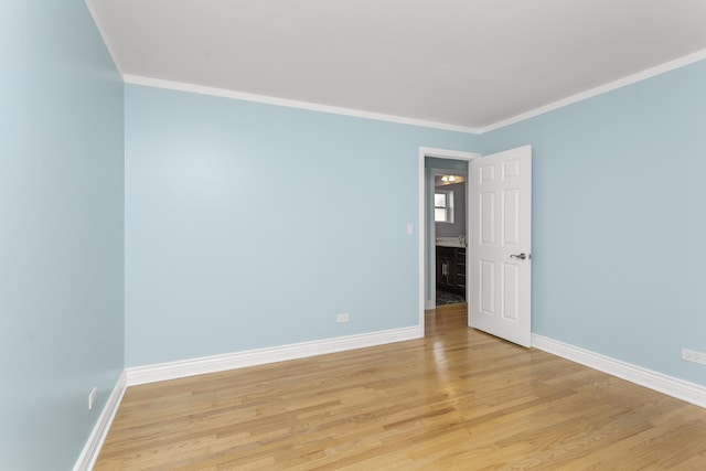 spare room featuring baseboards, light wood-type flooring, and ornamental molding