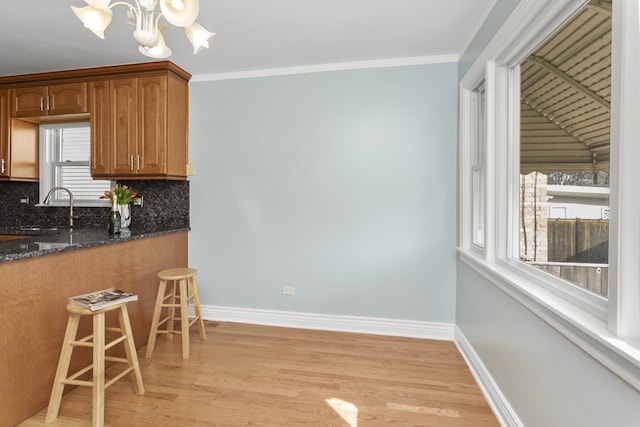 kitchen featuring decorative backsplash, dark stone countertops, baseboards, and a sink