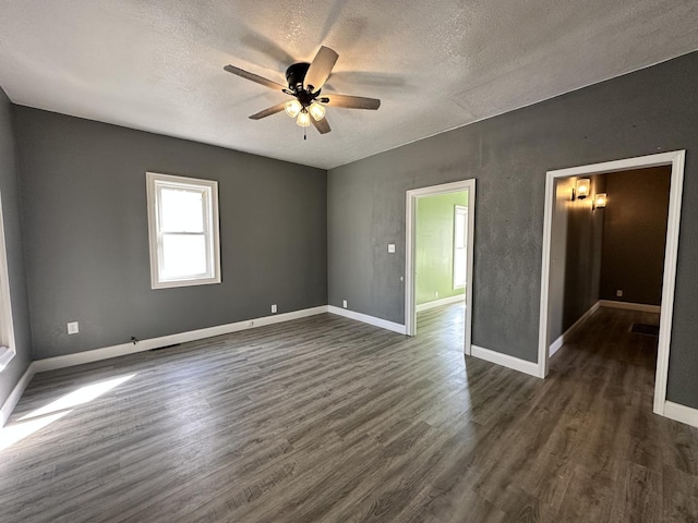empty room with a textured ceiling, dark wood-style floors, baseboards, and ceiling fan