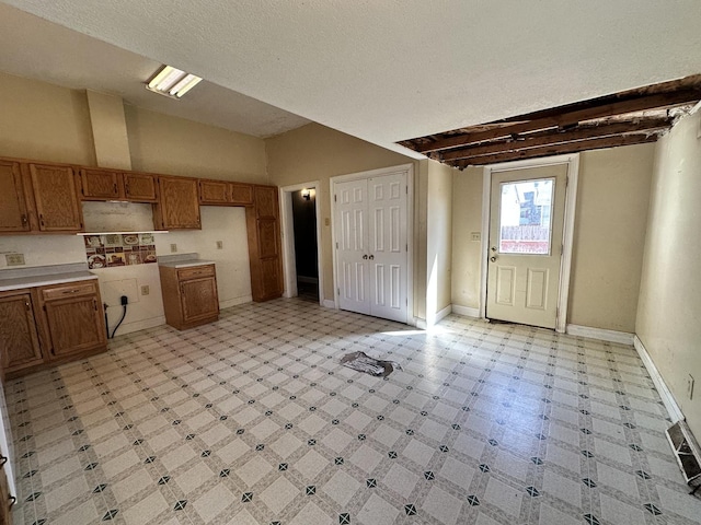 kitchen with baseboards, brown cabinets, light floors, and lofted ceiling