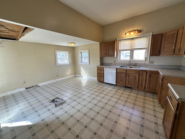 kitchen with baseboards, light floors, brown cabinets, white dishwasher, and a sink