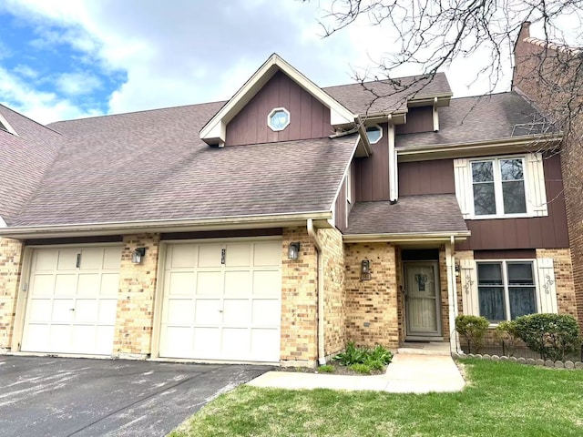 townhome / multi-family property with a garage, a shingled roof, driveway, board and batten siding, and brick siding
