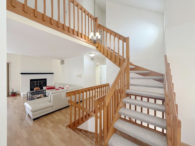 stairway featuring a high ceiling, a chandelier, a brick fireplace, visible vents, and wood finished floors