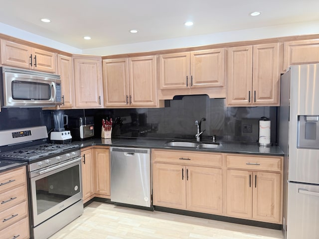kitchen with light brown cabinetry, dark countertops, appliances with stainless steel finishes, and a sink