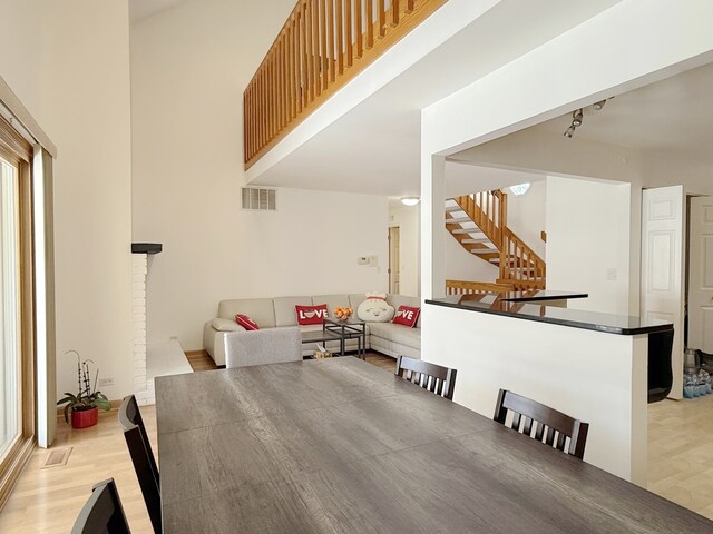 dining space featuring a towering ceiling, stairs, visible vents, and wood finished floors