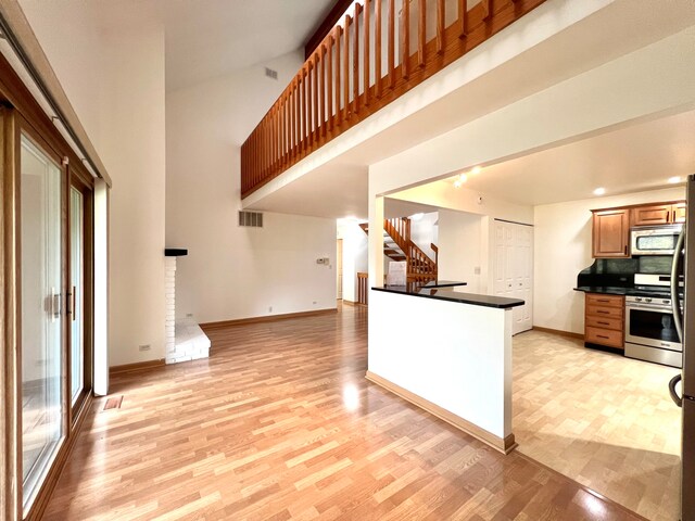 kitchen with appliances with stainless steel finishes, dark countertops, baseboards, open floor plan, and light wood finished floors