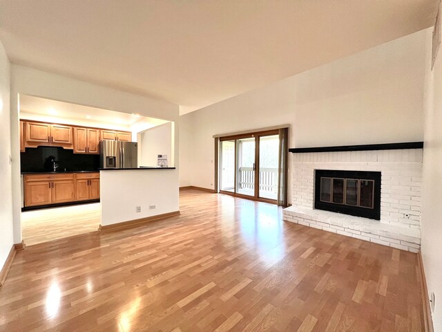 unfurnished living room featuring a fireplace, a sink, light wood-style flooring, and baseboards