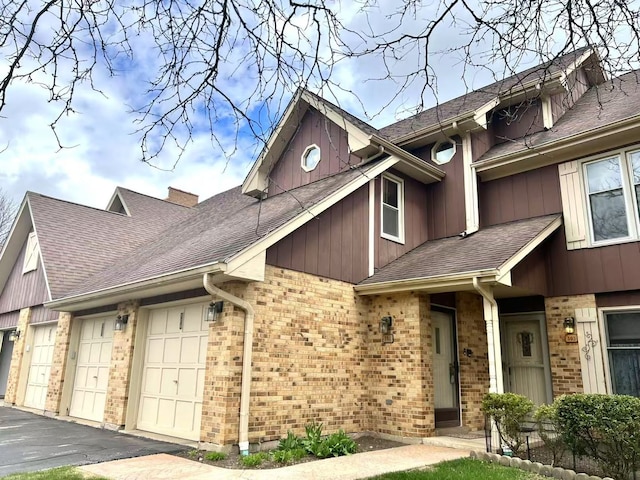 exterior space with a chimney, brick siding, a garage, driveway, and roof with shingles