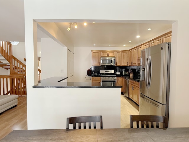 kitchen with appliances with stainless steel finishes, dark countertops, light wood-style floors, recessed lighting, and a peninsula