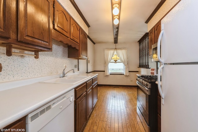 kitchen with white appliances, wallpapered walls, light wood-style flooring, a sink, and hanging light fixtures