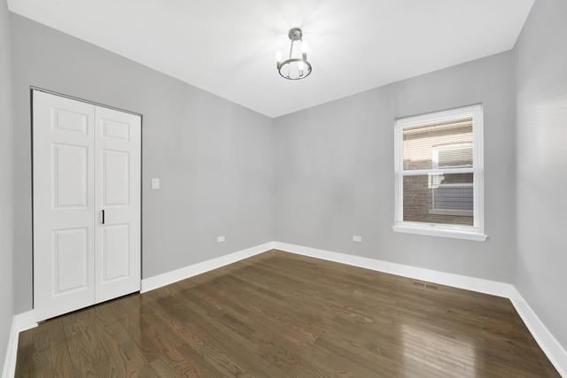 unfurnished room featuring an inviting chandelier, baseboards, and dark wood-style flooring