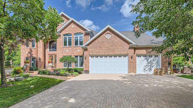 traditional home with brick siding, roof with shingles, a chimney, decorative driveway, and a garage