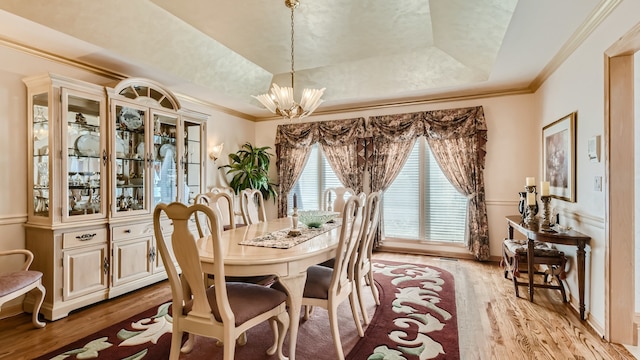 dining space with crown molding, a notable chandelier, light wood finished floors, and a tray ceiling