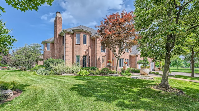 view of front of house with brick siding, a chimney, and a front yard