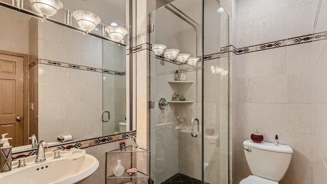full bath with tile walls, toilet, a stall shower, and a sink