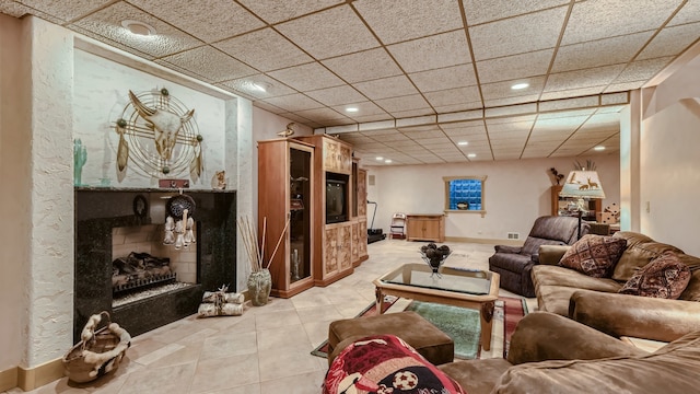 living room featuring light tile patterned floors, baseboards, a paneled ceiling, and a fireplace