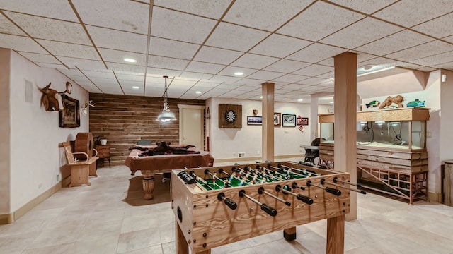 game room featuring recessed lighting, a drop ceiling, baseboards, and wood walls