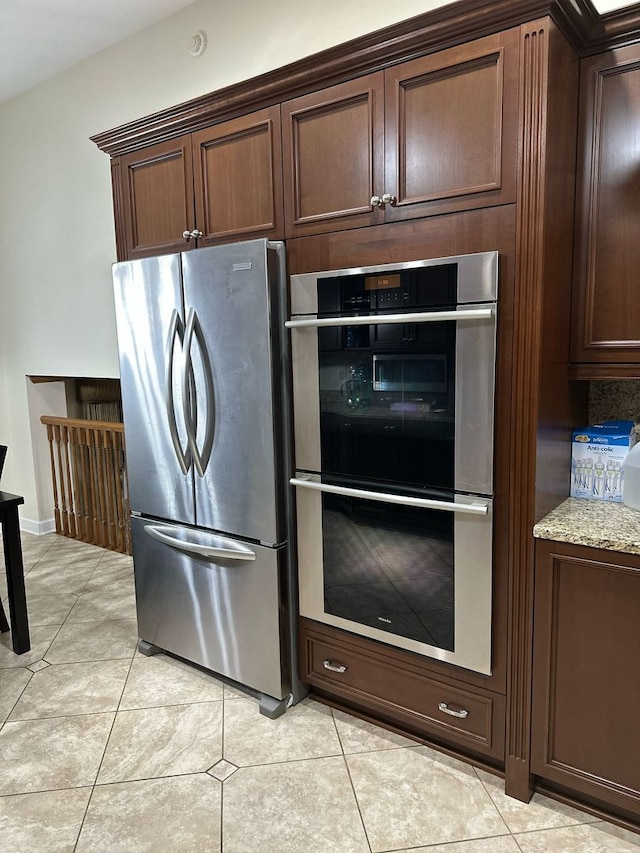 kitchen with dark brown cabinets, light stone countertops, appliances with stainless steel finishes, and light tile patterned floors