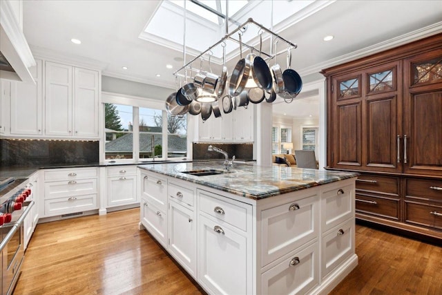 kitchen featuring a sink, a skylight, dark stone countertops, ornamental molding, and backsplash