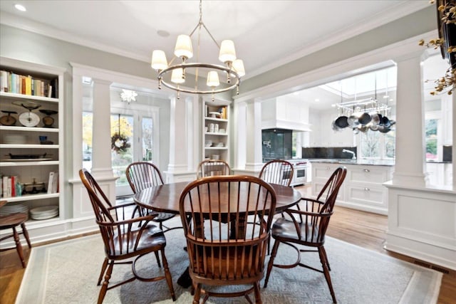 dining space with ornamental molding, built in features, a chandelier, wood finished floors, and ornate columns