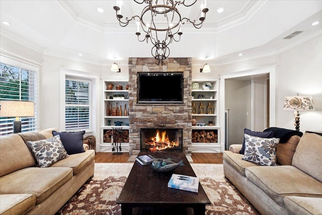 living area with wood finished floors, a notable chandelier, visible vents, a stone fireplace, and ornamental molding