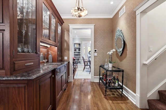 bar with hanging light fixtures, a sink, crown molding, dark wood finished floors, and baseboards