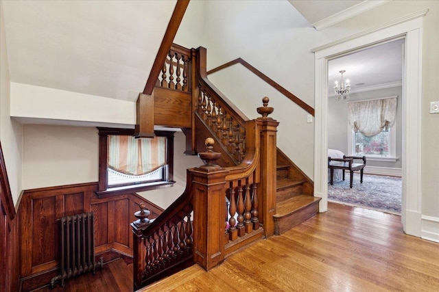 stairs with ornamental molding, radiator, a notable chandelier, and wood finished floors