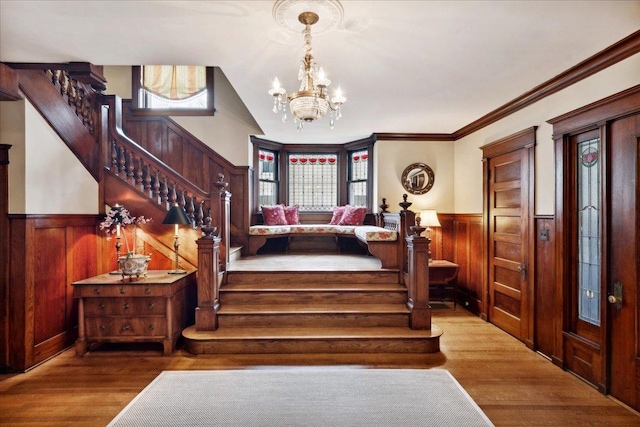 stairway with wood finished floors, wooden walls, wainscoting, a chandelier, and ornamental molding
