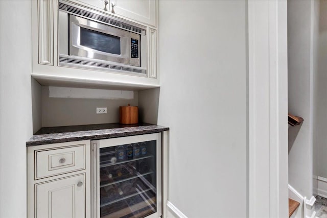 bar featuring wine cooler, baseboards, a bar, and stainless steel microwave