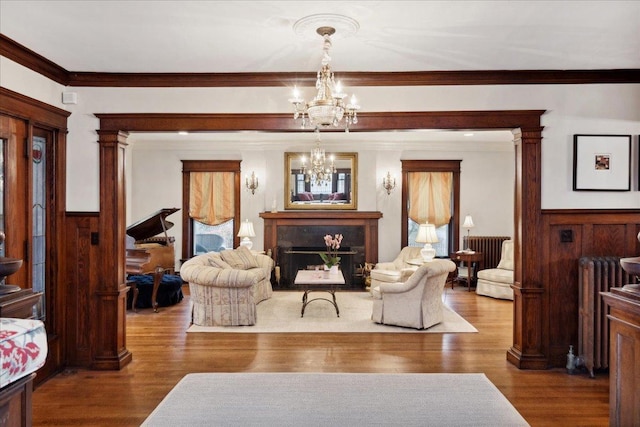 living area featuring wood finished floors, radiator heating unit, decorative columns, crown molding, and a notable chandelier