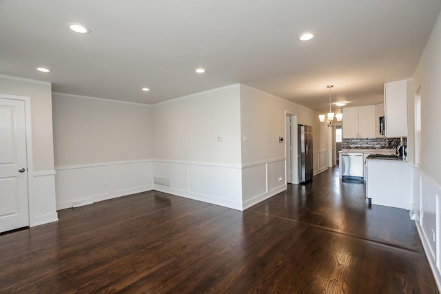 unfurnished living room featuring recessed lighting, a wainscoted wall, dark wood-type flooring, and a chandelier