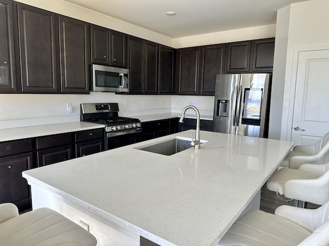 kitchen with a breakfast bar, a kitchen island with sink, a sink, light stone counters, and appliances with stainless steel finishes