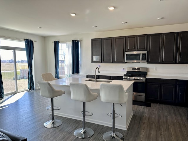 kitchen with a sink, stainless steel appliances, a breakfast bar, and dark wood-style floors