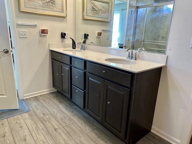 bathroom featuring double vanity, tiled shower, wood finished floors, and a sink