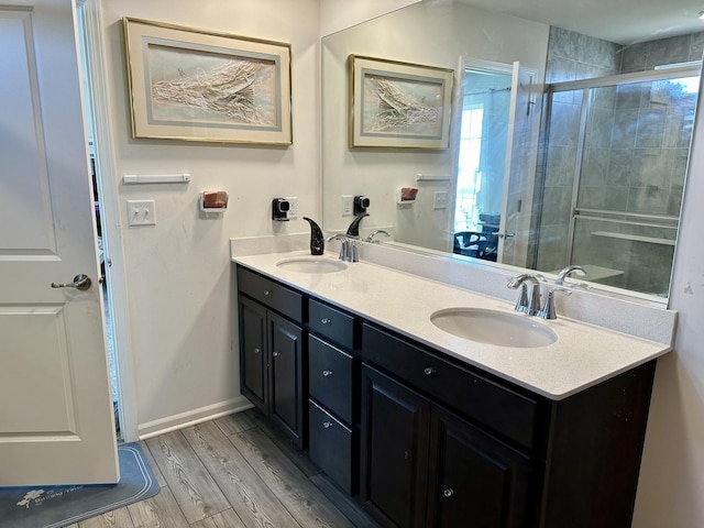 full bathroom featuring double vanity, a tile shower, wood finished floors, and a sink