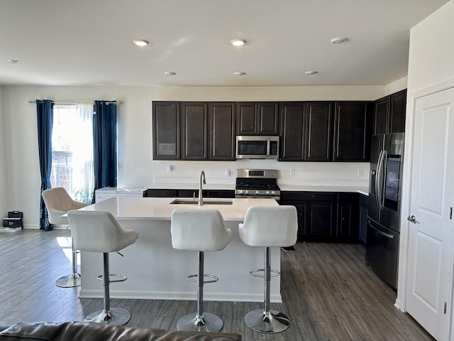 kitchen featuring dark wood-type flooring, a breakfast bar area, light countertops, stainless steel appliances, and a sink