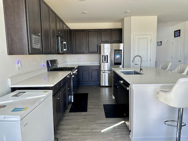 kitchen featuring a kitchen island with sink, light wood-style flooring, a sink, stainless steel appliances, and light countertops