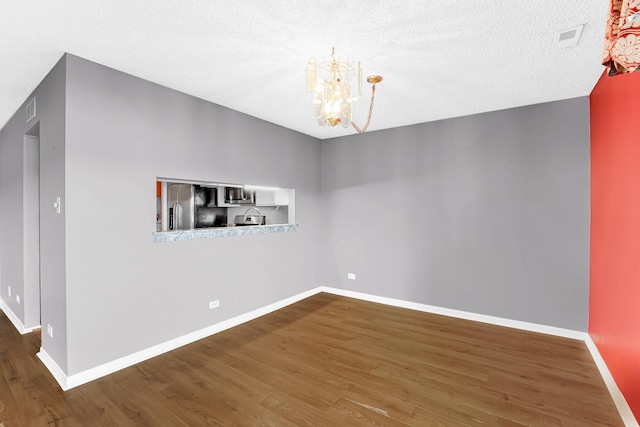 unfurnished dining area featuring visible vents, baseboards, wood finished floors, a notable chandelier, and a textured ceiling