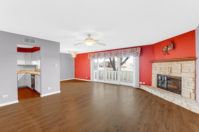 unfurnished living room featuring visible vents, ceiling fan, a stone fireplace, dark wood-style flooring, and a sink