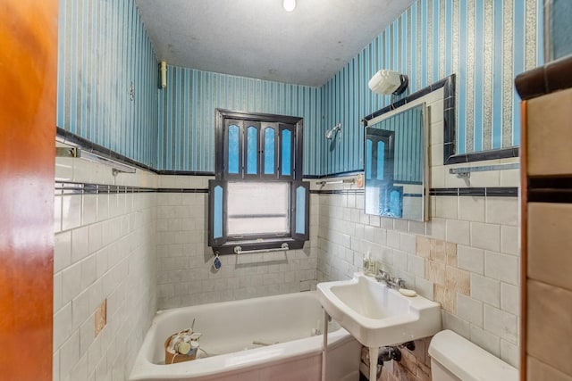 bathroom featuring wallpapered walls, toilet, a bathtub, wainscoting, and tile walls