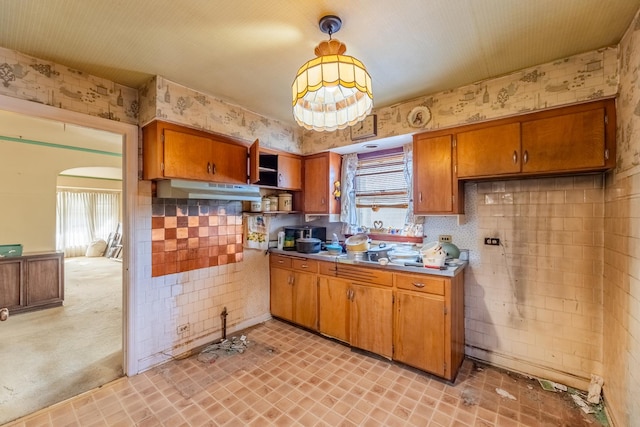 kitchen featuring under cabinet range hood, open shelves, brown cabinets, and wallpapered walls