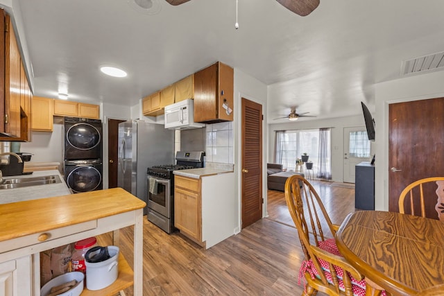 kitchen with stacked washer / dryer, ceiling fan, stainless steel appliances, a sink, and wood finished floors